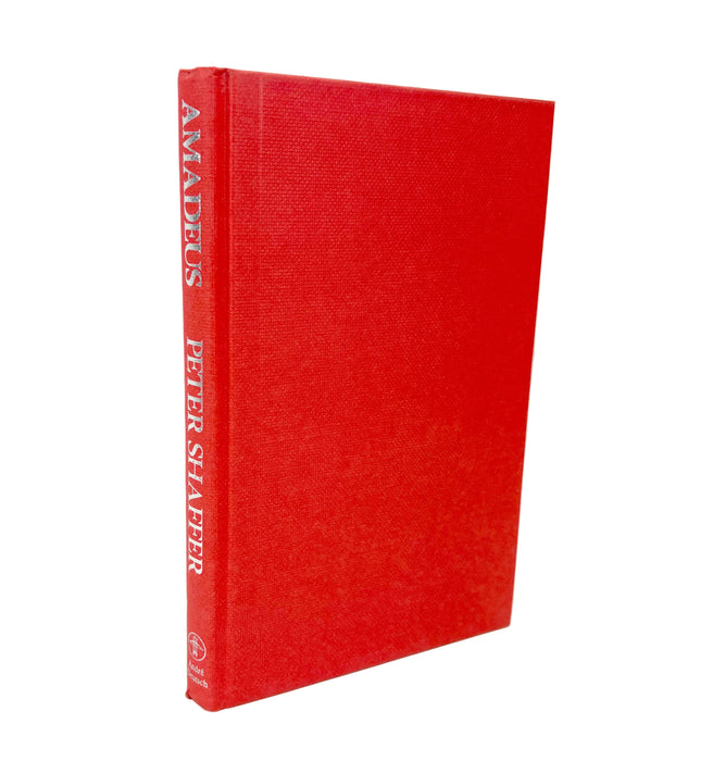A hardcover book titled 'AMADUS' by Peter Shaffer, standing upright at a slight angle. The book features a textured red cloth cover with the title and author name printed in white on the spine, set against a plain white background.