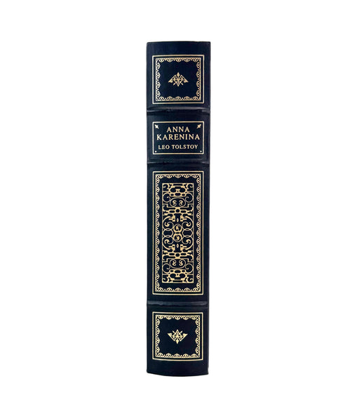 A single hardcover book standing upright on a white background, showing its dark navy blue spine with ornate gold decorative panels and the title text 'ANNA KARENINA LEO TOLSTOY'.