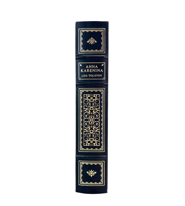 A single hardcover book standing upright on a white background, showing its dark navy blue spine with ornate gold decorative panels and the title text 'ANNA KARENINA LEO TOLSTOY'.