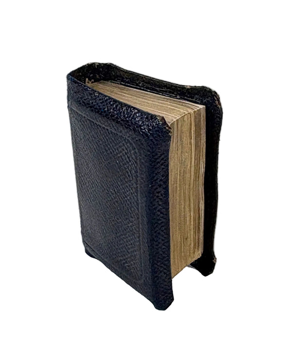 A miniature black faux-leather book cover or miniature book with textured black faux leather on the front and spine, showing aged beige pages, set against a plain white background.