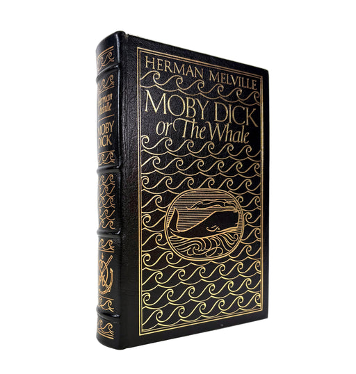 A vintage hardcover edition of Herman Melville's Moby Dick, featuring a black leather-like cover with ornate gold foil wave patterns and gold lettering, shown standing upright on a white background.