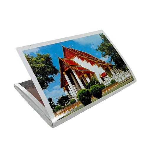 A stack of printed postcards or photo cards shown at an angle on a plain white background, with the top card displaying a colorful photograph of a Thai-style temple building under a blue sky.