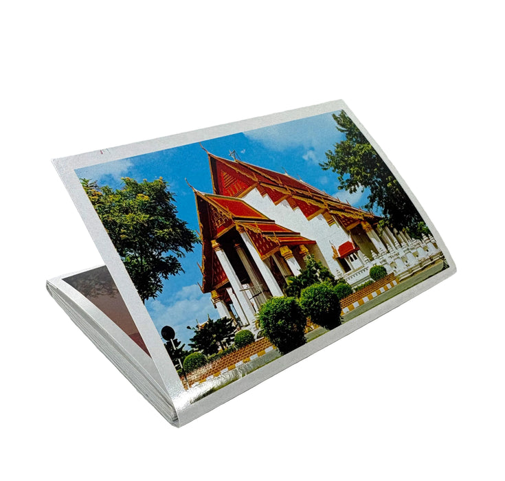 A stack of printed postcards or photo cards shown at an angle on a plain white background, with the top card displaying a colorful photograph of a Thai-style temple building under a blue sky.