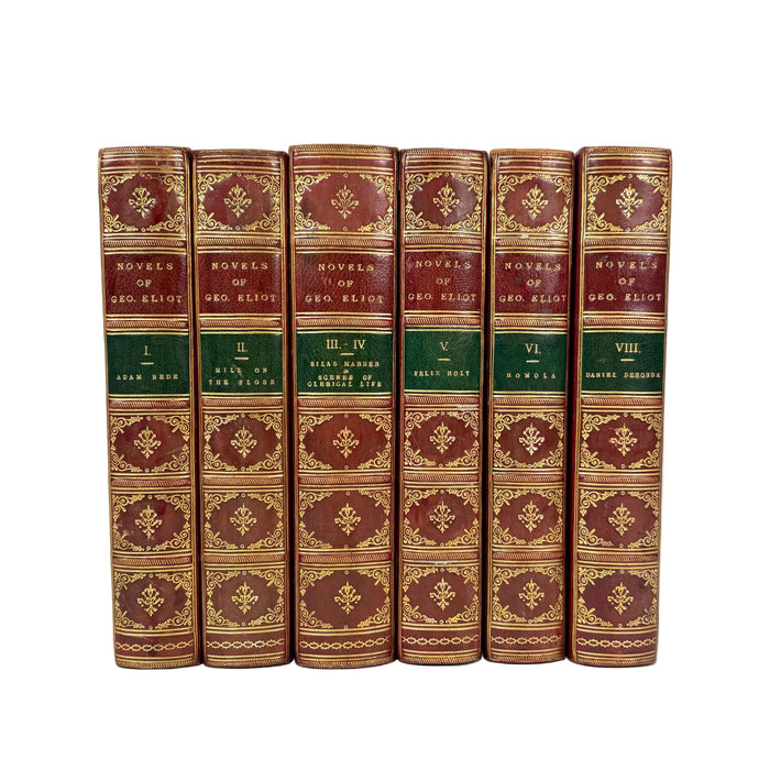 A set of eight hardcover books from the 'Novels of Geo. Eliot' series, bound in dark reddish-brown leather with ornate gold gilding and green title bands, displayed upright against a plain white background.