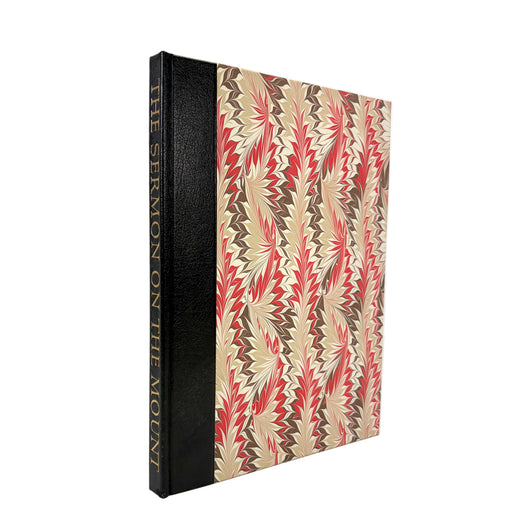 A hardcover book titled 'THE SERMON ON THE MOUNT' standing upright at a slight angle. The book spine is black with gold lettering, and the front cover features a geometric zigzag pattern in beige, brown, and red.