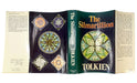 An open hardcover book showing the front cover, spine, and inner pages of 'The Silmarillion' by Tolkien. The cover features a dark green background with a large multicolored circular emblem and the title in orange and white text.